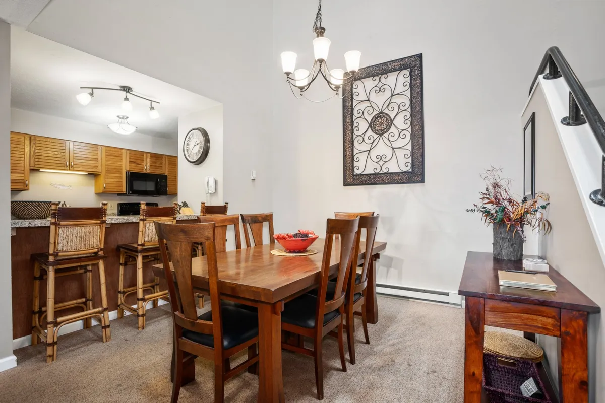 The dining area is showcased with a large wooden table under a stylish chandelier, surrounded by comfortable seating, and positioned near the entrance to the kitchen. Artistic wall decor and warm tones foster a welcoming environment for shared meals and gatherings.