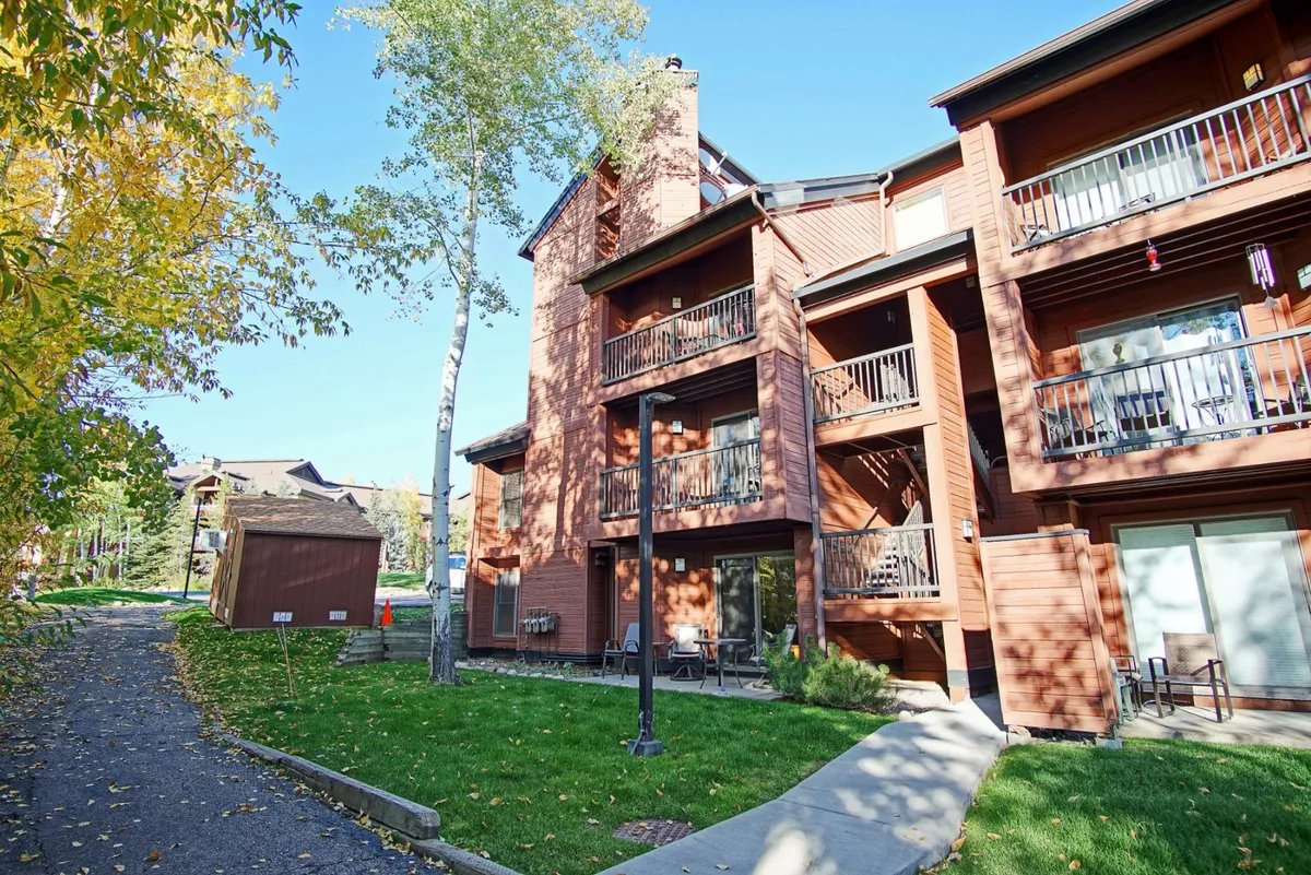 This exterior image features wooden balconies overlooking a green lawn, with a welcoming pathway leading directly to the property. The lush landscaping and open space evoke a sense of arrival and connection to the outdoors, while the balconies hint at a friendly, social environment.