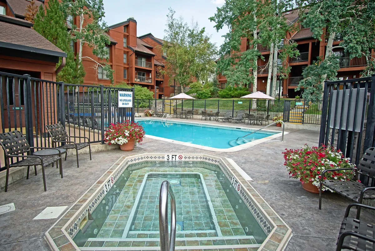This image features a vibrant outdoor swimming pool area with an adjacent jacuzzi, surrounded by lounge chairs and blooming flowers. The inviting setup suggests both relaxation and social opportunities, ideal for guests enjoying seasonal amenities.