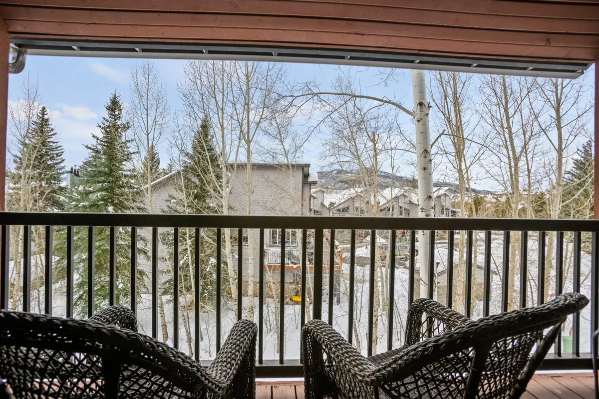 A peaceful balcony scene with wicker chairs overlooks snow-covered ground and surrounding trees, offering a tranquil spot to relax and enjoy the mountain air. The inviting arrangement encourages quiet mornings or evening conversations with scenic views.