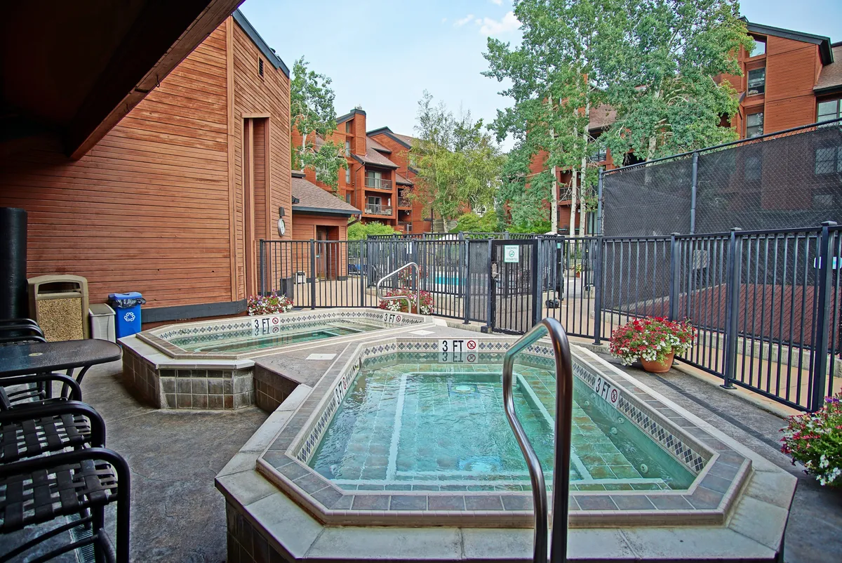 This exterior shot focuses on a cluster of inviting hot tubs within a fenced area, surrounded by greenery. The setting suggests warmth and relaxation, especially after a day on the slopes, and is ideal for social gatherings or family time.