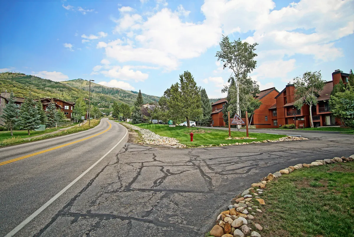 A winding road leading toward a mountain backdrop, with tree-lined areas and buildings featuring red accents. The tranquil setting evokes adventure and exploration, inviting guests to imagine hiking, biking, or simply soaking in mountain scenery.