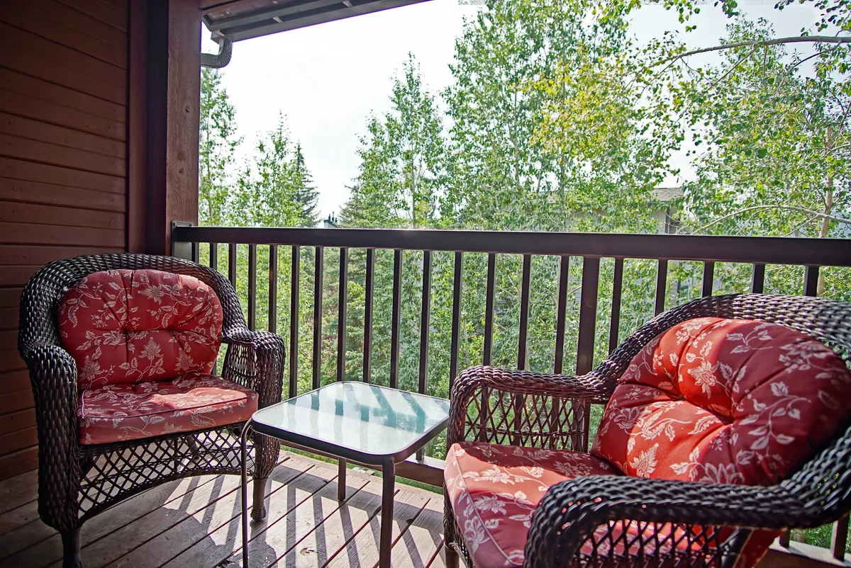 An inviting outdoor seating area with woven chairs featuring floral cushions and a glass-topped table, surrounded by greenery. The setting is ideal for quiet morning coffees or winding down after a night out downtown, capturing both relaxation and socialization.