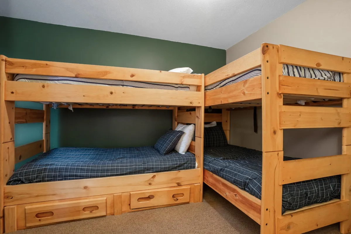 A playful bunk room featuring two sturdy sets of bunk beds, plaid bedding, and a cheerful green accent wall. The room is styled for kids or groups, encouraging fun, togetherness, and memorable sleepovers.