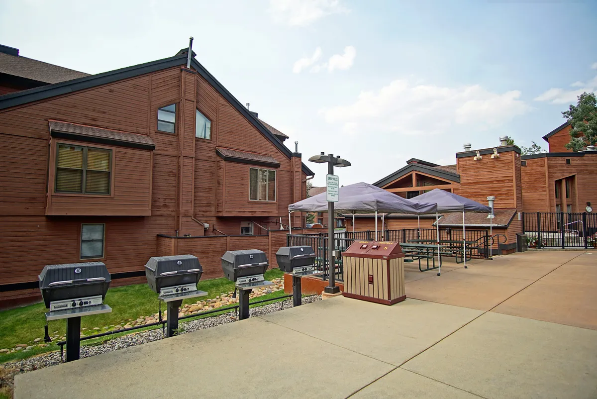 The image highlights a community outdoor area with BBQ grills and picnic tables set against the backdrop of the building's façade. The setup promises memorable gatherings, summer cookouts, and a communal atmosphere.